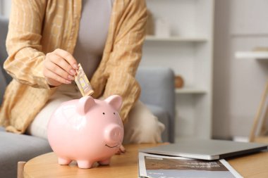 Genç bir kadın evdeki masadaki kumbaraya avroluk banknot yatırıyor.