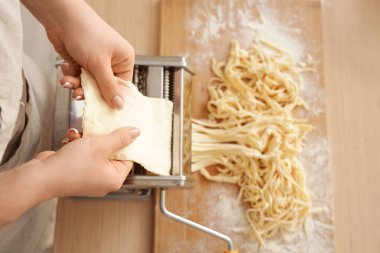 Mutfaktaki masada makineyle makarna yapan genç bir kadın.