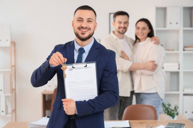 Ev kiralama sözleşmesi olan erkek emlakçı ve ofisteki çifte karşı ev anahtarı.