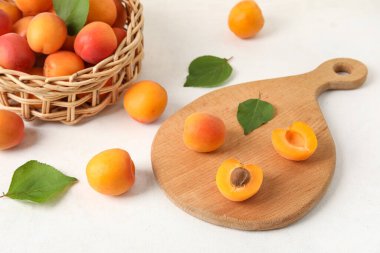 Tahta ve hasır kasede beyaz masada taze kayısılar var.