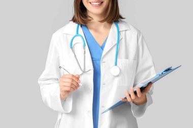 Gri arka planda steteskop ve panoya sahip mutlu kadın kardiyolog, yakın plan.