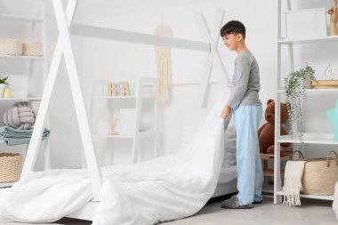 Pijamalı tatlı çocuk evde yatak yapıyor.