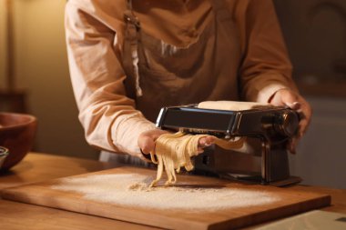 Genç bir kadın karanlık mutfakta makineyle makarna yapıyor, yakın plan.