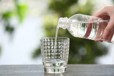 Kadın şişeden bardağa temiz su dolduruyor.