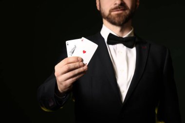 Koyu yeşil arka planda poker kartları olan yakışıklı genç adam, yakın plan.