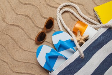 Arka planda plaj aksesuarları, defter ve güneş kremi olan yaz çantası.