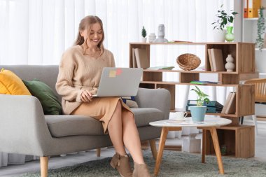 Ofisteki kanepede dizüstü bilgisayarla çalışan kadın web tasarımcısı.