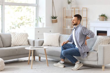 Evdeki kanepede sırt ağrısı çeken genç bir adam.