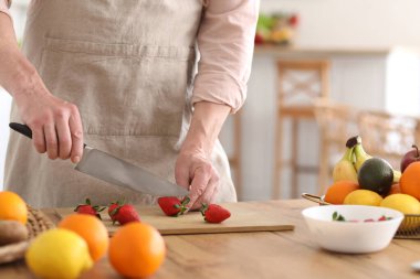 Olgun bir adam mutfakta meyve suyu için çilek kesiyor, yakın plan.