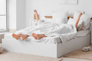 Yatak odasında battaniyenin altında kahve içen genç bir çift.