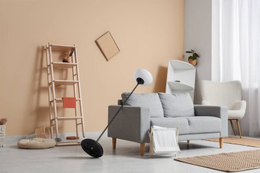 Gri kanepeli dağınık oturma odasının içi, standart lambayı ters çevirmiş ve depremden sonra rafları eğmiş.