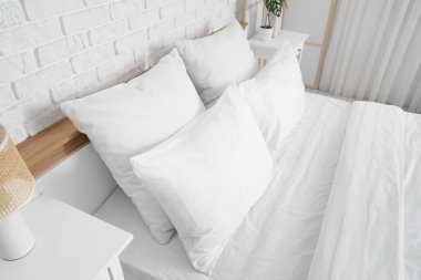 Beyaz battaniyeli rahat yatak ve şık yatak odasında yumuşak yastıklar, yakın çekim.