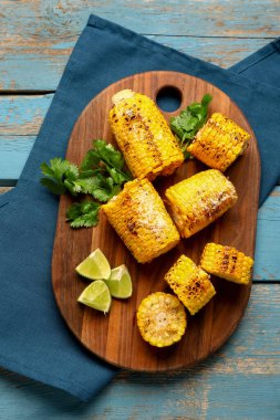 Lezzetli ızgara mısır koçanları ve mavi ahşap arka planda maydanozlu tahta.
