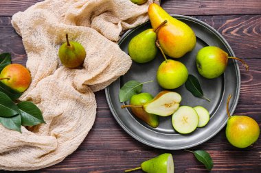 Koyu ahşap masada olgun armutlarla dolu bir tabak.