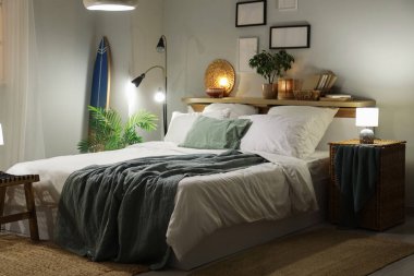 Şık bir yatak odası, yatak odası, sörf tahtası, parlayan lambalar ve akşamları raflarda ev dekorasyonu.