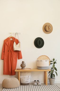 Salonun içinde askıda bank, çanta ve turuncu palto var.