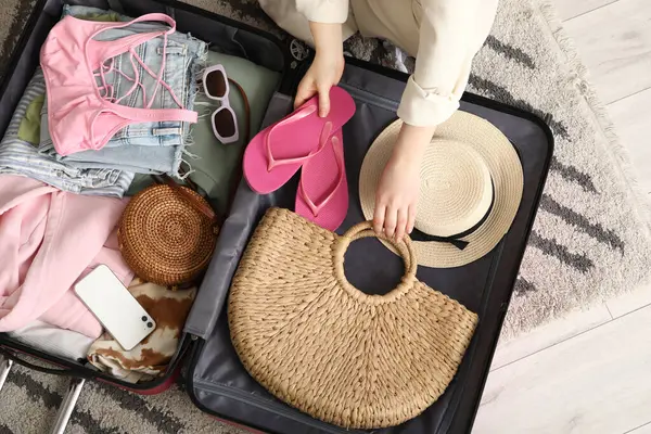 Otel odasında bavulunu elbiseleriyle ve çantasıyla boşaltan genç bir kadın.