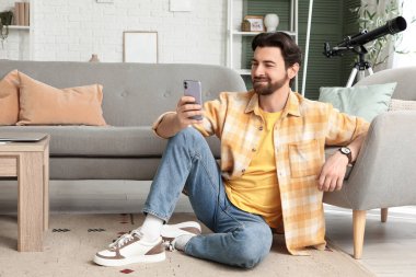 Evdeki halıda cep telefonu kullanan yakışıklı adam.
