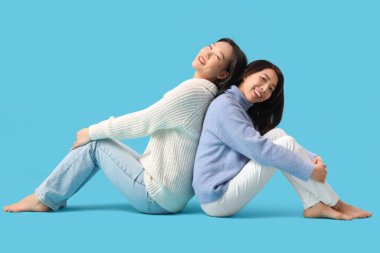 Güzel, mutlu Asyalı kız kardeşler mavi arka planda oturuyor.