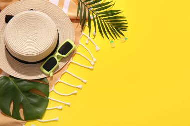 Sarı arka planda plaj aksesuarları ve tropikal yaprakları olan kompozisyon