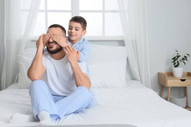 Pijamalı mutlu çocuk evde babasının gözlerini kapatıyor.