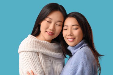 Güzel, mutlu Asyalı kız kardeşler mavi arka planda sarılıyorlar.