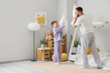 Pijamalı mutlu baba oğluyla yastık savaşı yapıyor.