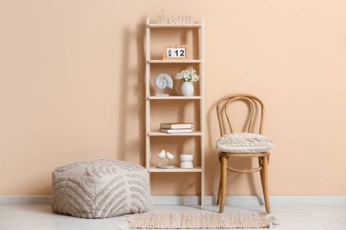 Oturma odasının içinde sandalye, puf, ahşap takvim, ev dekorasyonu ve vazolar bej duvarın yanındaki raflarda.