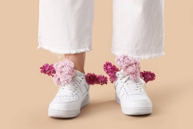 Bej arka planda ayakkabı giymiş leylak çiçekli genç kadın bacakları.