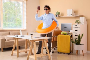 Yüzme yüzüğü ve pasaportu olan genç işadamı yaz tatilini ofisinde bekliyor.