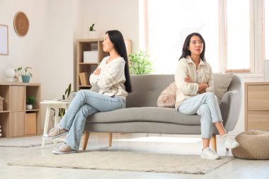 Evdeki kanepede oturan güzel üzgün Asyalı kız kardeşler.