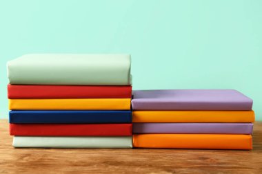 Turkuaz arka plana karşı ahşap masadaki renkli kitap yığınları