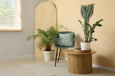 Kahve masası, sandalye ve bitkiler odanın içindeki bej duvarın yanında.