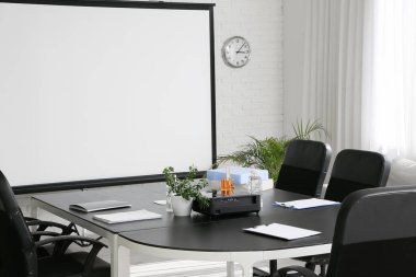 Modern ofiste masa, ev bitkileri ve projektör ekranlı konferans salonu.