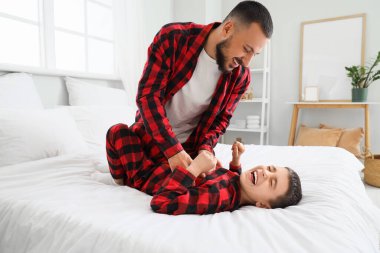 Kareli pijamalı mutlu bir baba oğluyla evde yatakta eğleniyor.