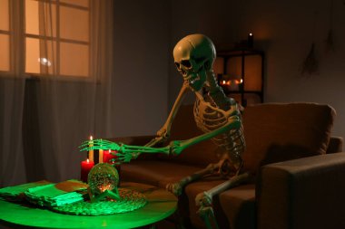 Kristal küreli iskelet ve karanlık oturma odasında yanan mumlar.