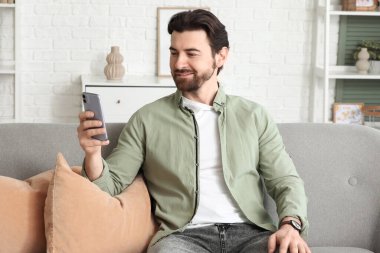 Evdeki koltukta cep telefonu kullanan yakışıklı adam.