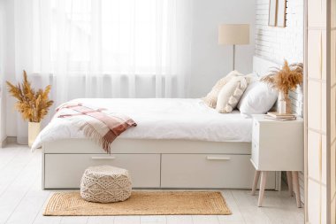 Büyük bir yatağı, masası ve vazolarında otları olan ışık odasının içi.