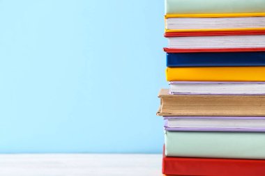 Mavi arkaplana karşı beyaz ahşap masa üzerinde renkli kitap yığını