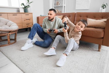 Mutlu baba ve oğlu evdeki kahverengi deri kanepenin yanında video oyunu oynuyorlar.