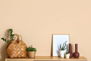 Üzerinde bitkiler ve çerçeve olan hasır sepetler bej duvarın yanında.