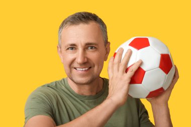 Sarı arka planda futbol topuyla oynayan yakışıklı olgun bir adam.