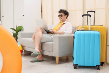 Genç iş adamı ofisteki kanepede dizüstü bilgisayar kullanıyor. Yaz tatili