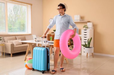 Yüzme yüzüğü ve bavulu olan genç işadamı yaz tatilini ofiste bekliyor.