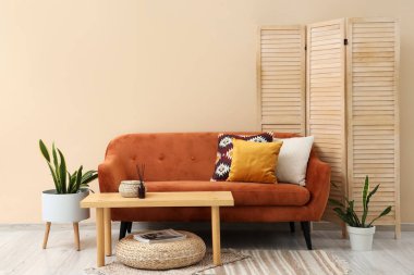 Konforlu kahverengi kanepe, masa ve katlanan ekran oturma odasının iç tarafındaki bej duvarın yanında.