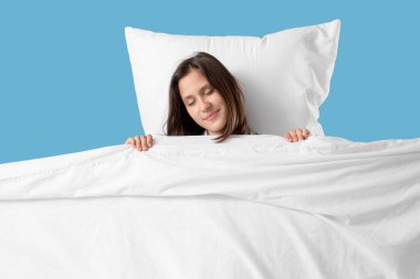 Yastıklı ve battaniyeli genç bir kadın mavi arka planda uyuyor.