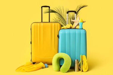 Plaj aksesuarları, termos, kulaklık ve sarı arka planda palmiye yaprakları olan bavullar.