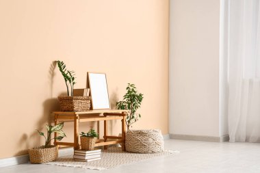 Ahşap bank, çerçeve ve hasır sepetler. Odada bej duvarın yanında bitkiler var.