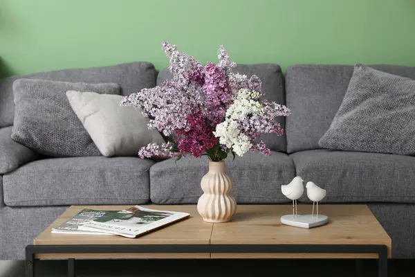 İçinde leylak çiçekleri, dergiler ve dekorasyon olan vazo oturma odasında.