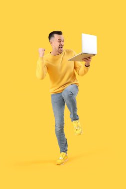 Sarı arka planda dizüstü bilgisayarı olan mutlu genç adam.